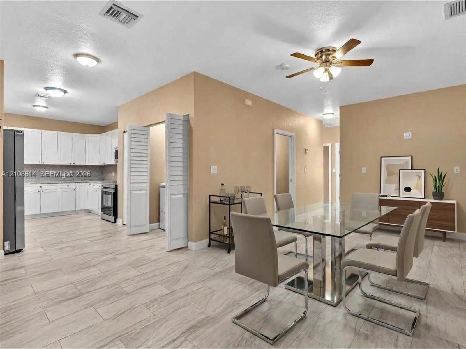 Open-concept interior featuring light tile flooring, white cabinetry, louvered closet doors, and a ceiling fan