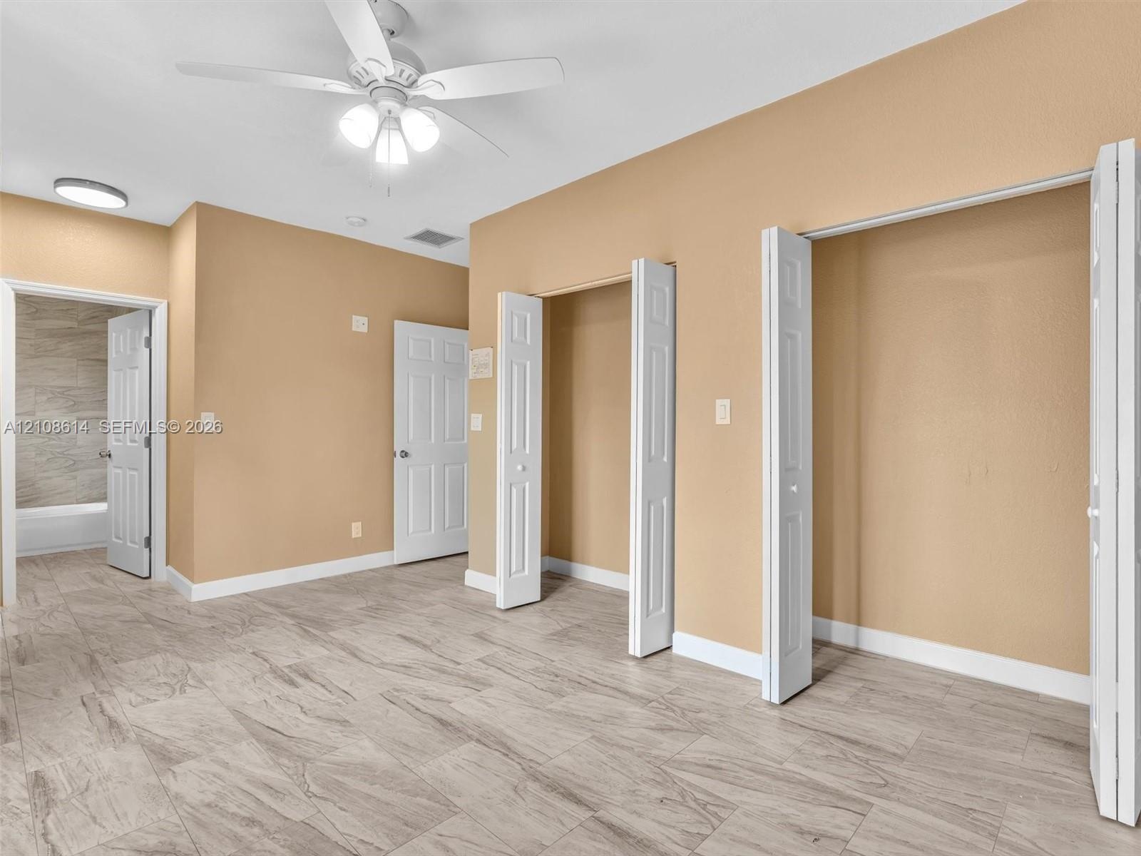 Room featuring wood-finish tile flooring, dual bi-fold closets, a central ceiling fan with integrated lighting, and white six-panel interior doors