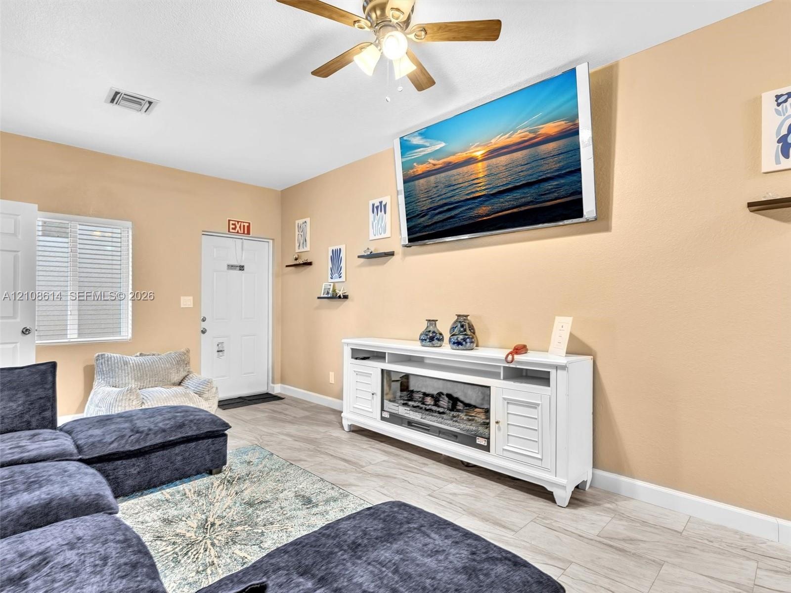 Neutral-toned interior space featuring wood-finish flooring, a ceiling fan with integrated lighting, and a white built-in media console with an electr