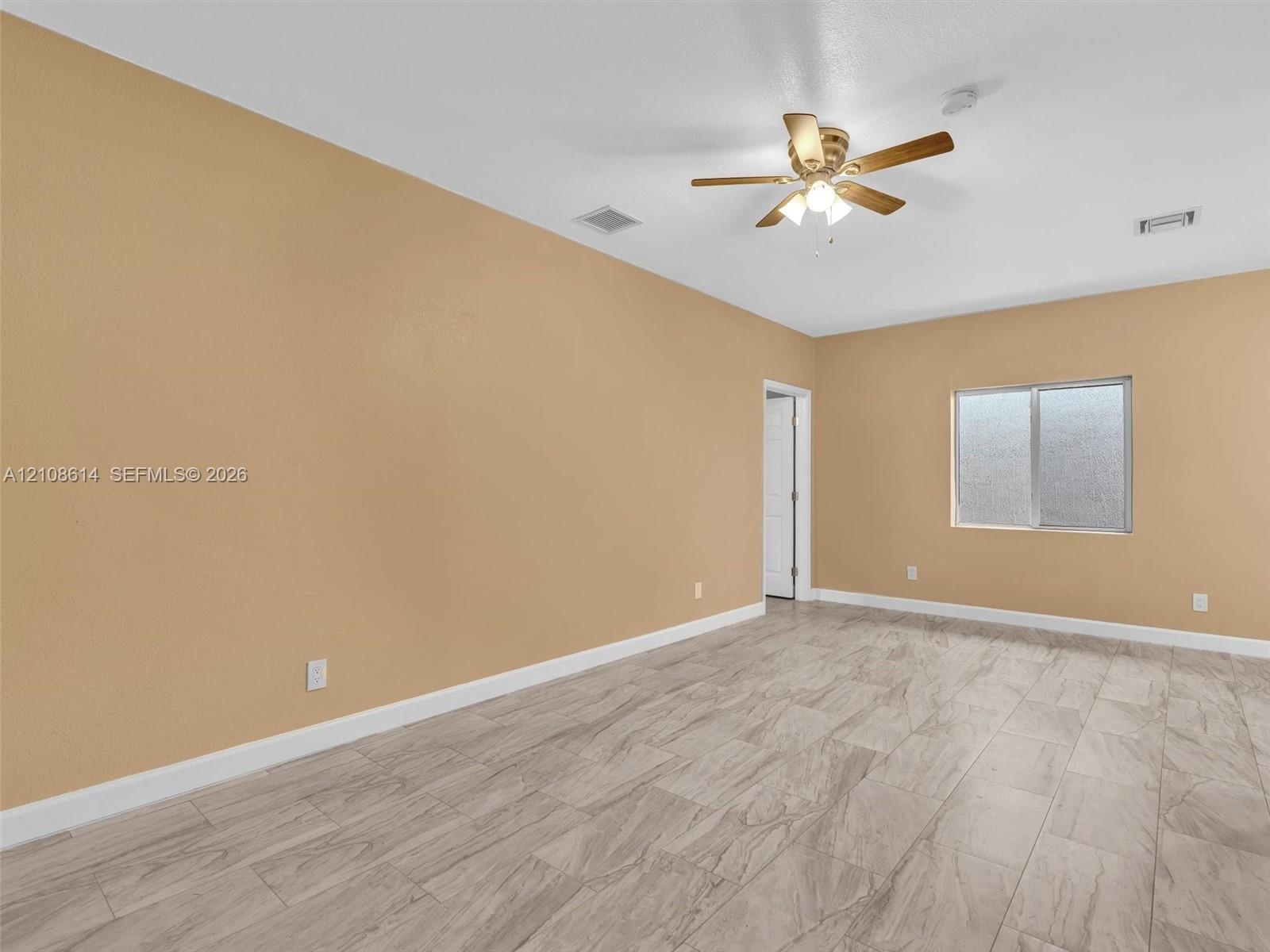 Neutral-toned interior space featuring stone-finish tile flooring, a multi-blade ceiling fan with integrated lighting, and a single-pane sliding windo