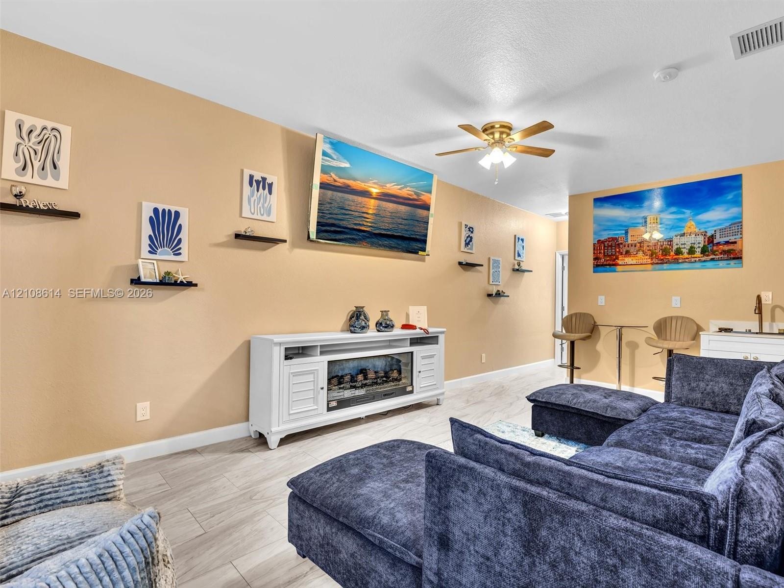 Neutral wall tones, wood-finish flooring, ceiling fan with integrated lighting, and white cabinetry featuring an electric fireplace insert