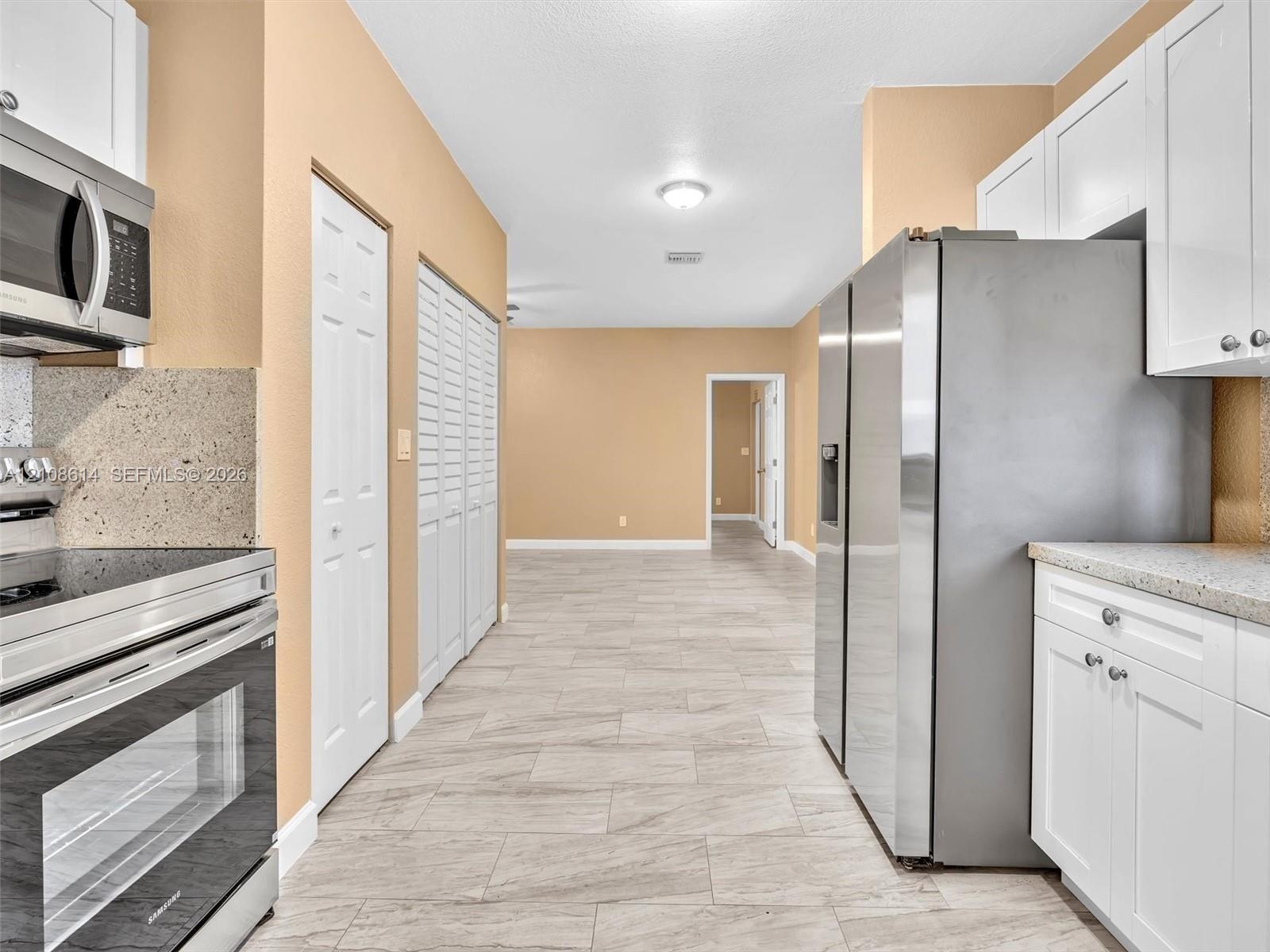 Kitchen featuring white cabinetry, stone-finish countertops, stainless steel appliances, and tile flooring