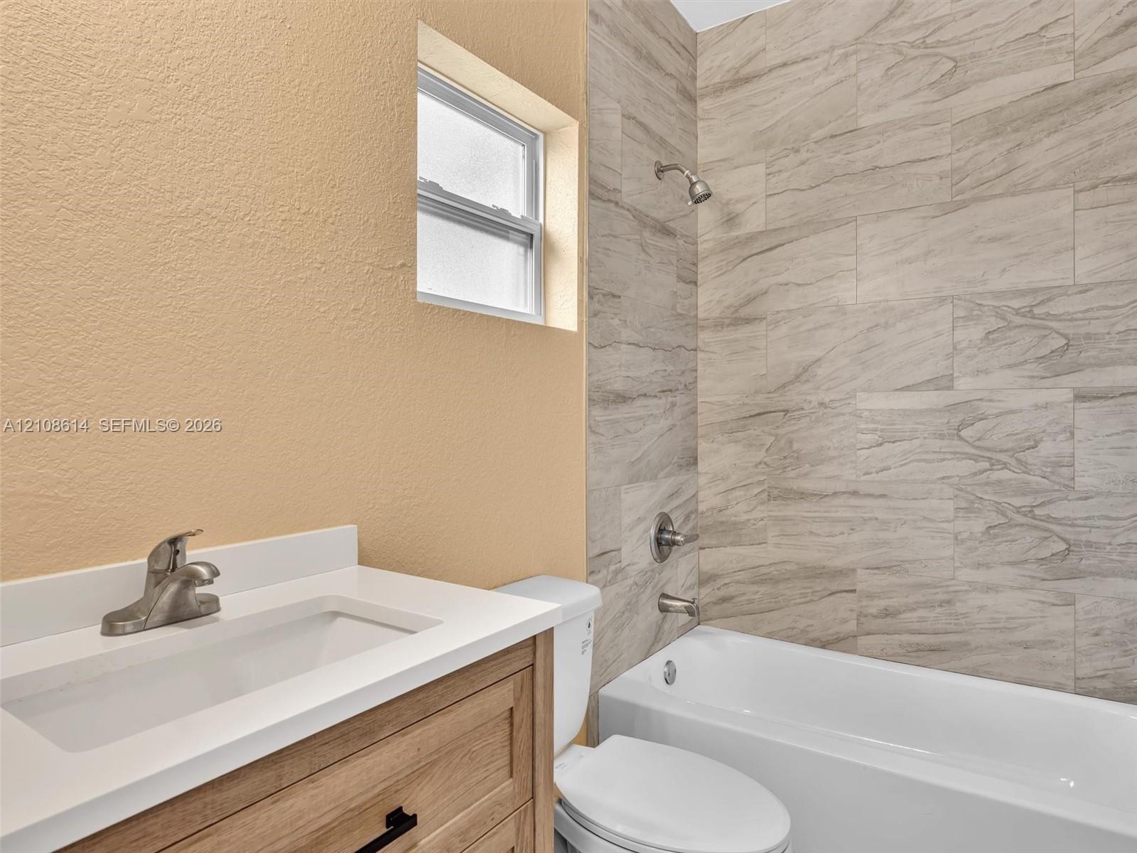 Vanity featuring a light wood-finish cabinet, white solid-surface countertop, and integrated sink, complemented by a tub-shower combination with large