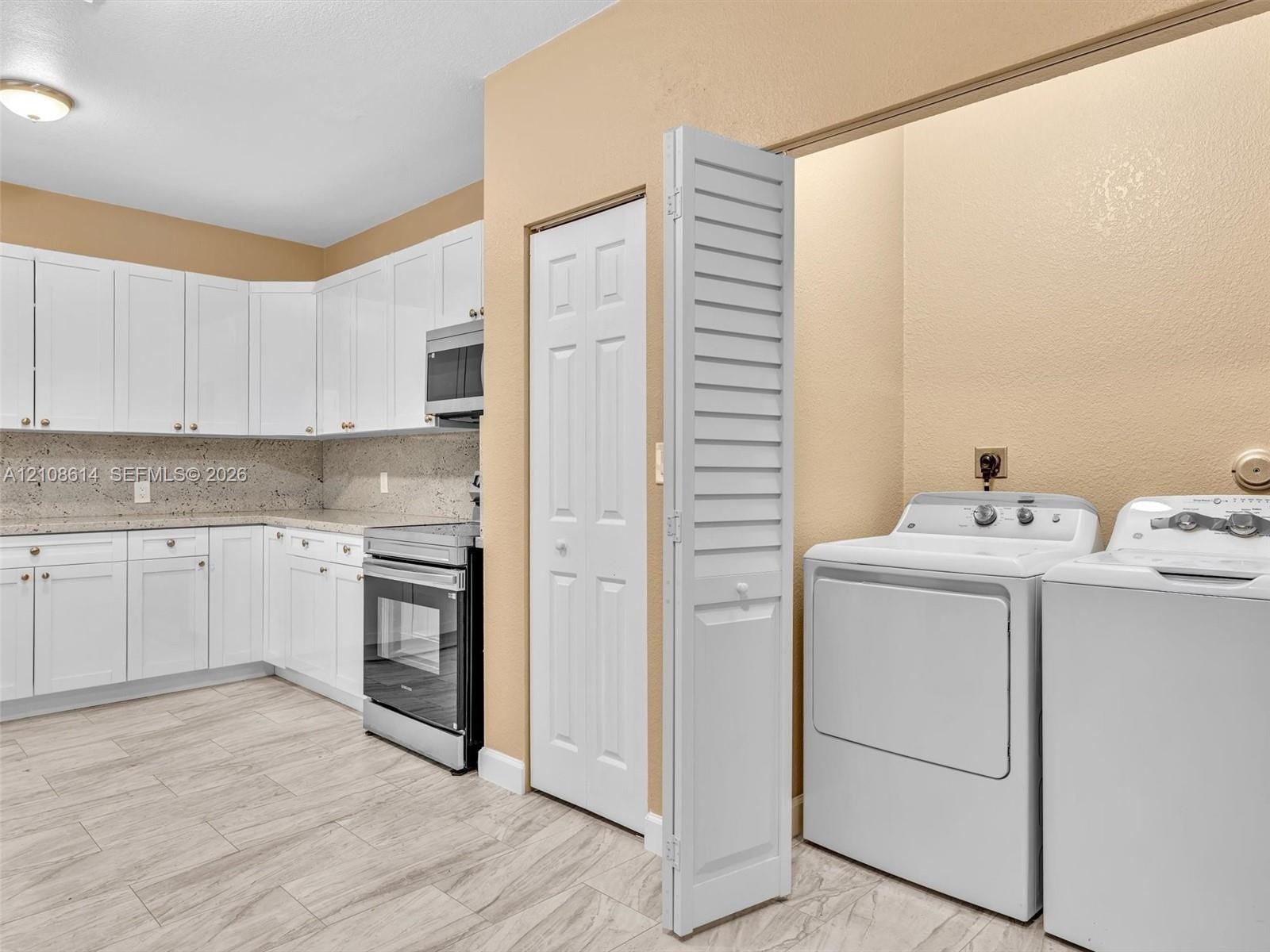 Kitchen featuring white cabinetry, stone-finish countertops, stainless steel appliances, wood-finish tile flooring, and a dedicated laundry area with 