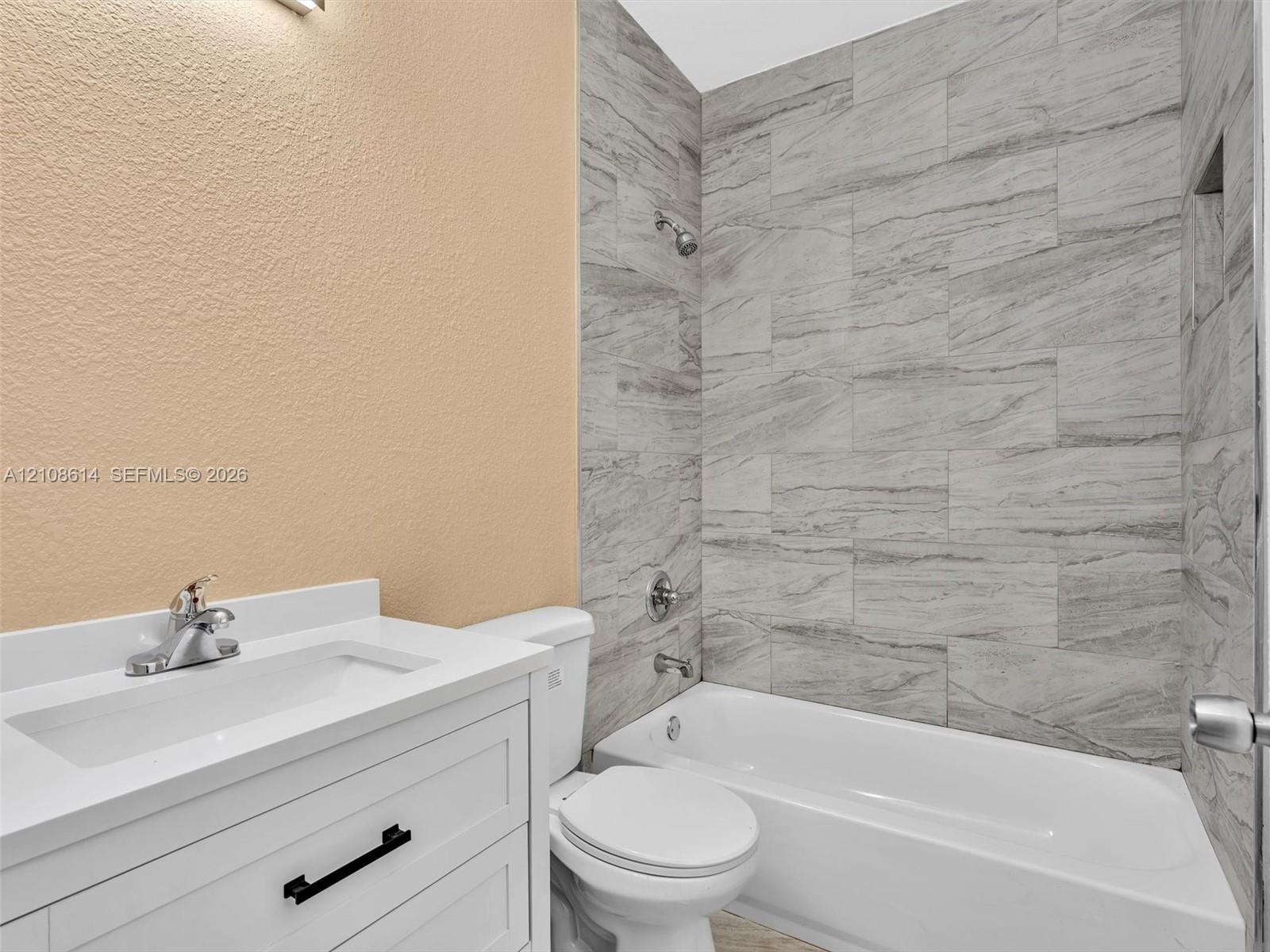 White vanity with a rectangular sink, matte black hardware, tiled shower surround with a built-in recessed niche, and polished metal fixtures