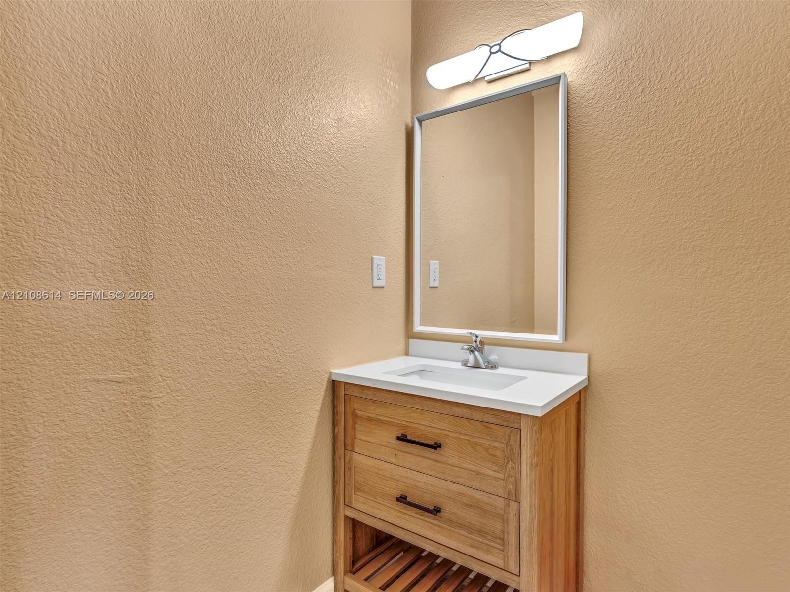 Wood-finish vanity featuring dual drawers, an open-slatted lower shelf, a white rectangular countertop with an integrated basin, and a framed mirror p