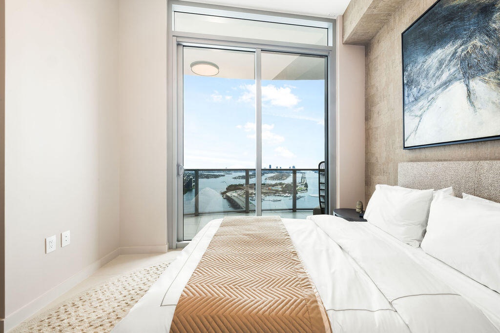 Floor-to-ceiling sliding glass door, exposed concrete structural beam, textured accent wall, and private balcony with railing