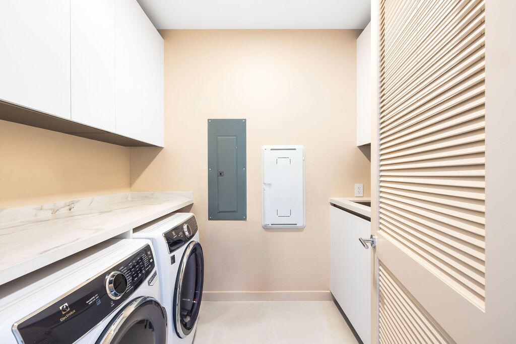 Laundry room featuring white shaker-style wall cabinetry, stone-finish countertops, and a louvered door