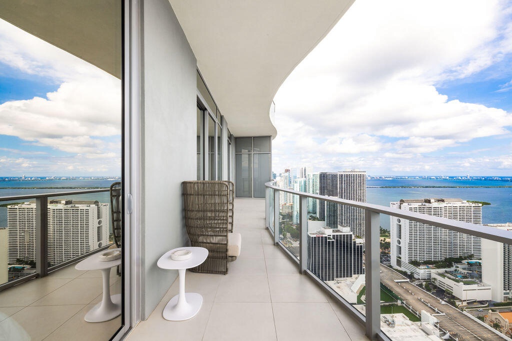 Expansive wrap-around balcony featuring large-format tile flooring, a curved architectural design, and floor-to-ceiling glass paneling with metal rail