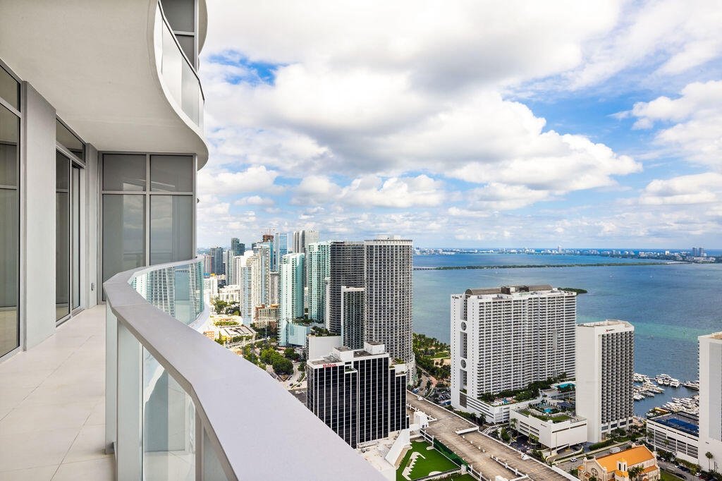Curved exterior balcony with glass railing, large-format tile flooring, and expansive floor-to-ceiling windows