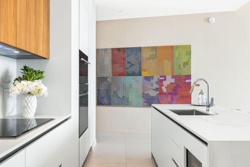 Kitchen featuring minimalist white cabinetry, wood-finish upper cabinets, integrated wall oven, white stone-surface countertops, and a stainless steel