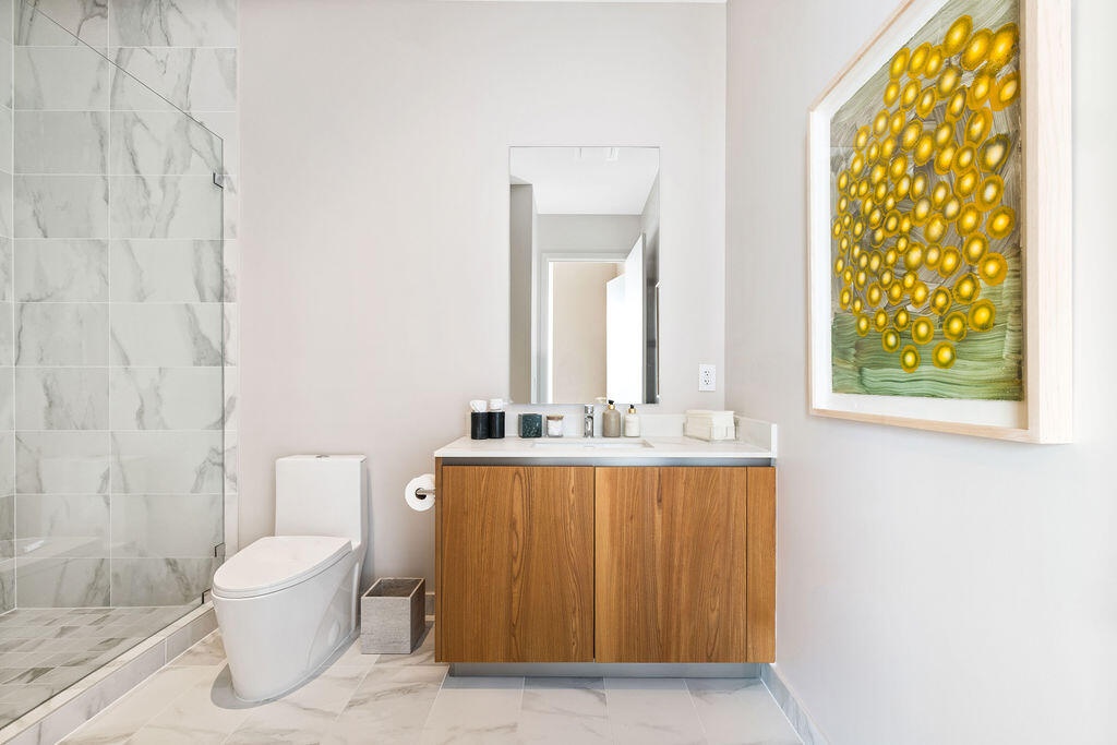 Bathroom featuring a wood-finish vanity with a stone countertop, a glass-enclosed shower with large-format tile surround, a wall-mounted mirror, and t