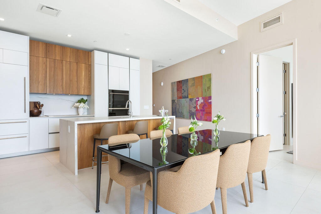 Modern kitchen featuring two-tone cabinetry with wood-finish uppers and white flat-panel base cabinets, central island with waterfall-edge countertop,