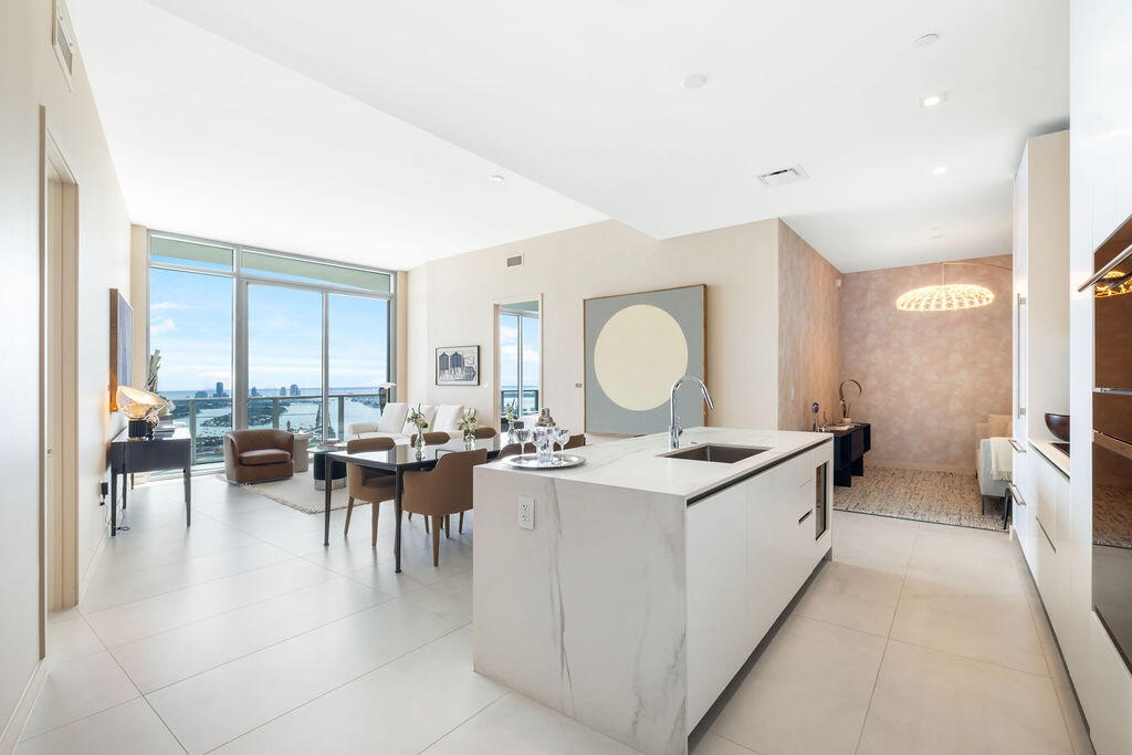 Open-concept interior featuring an oversized waterfall-edge stone island, floor-to-ceiling glass windows, high ceilings with recessed lighting, and ex