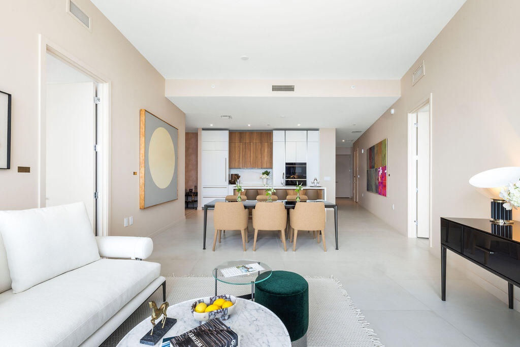 Open-concept interior featuring light-toned flooring, high ceilings, custom wood and white cabinetry, a built-in oven, and a kitchen island with stone