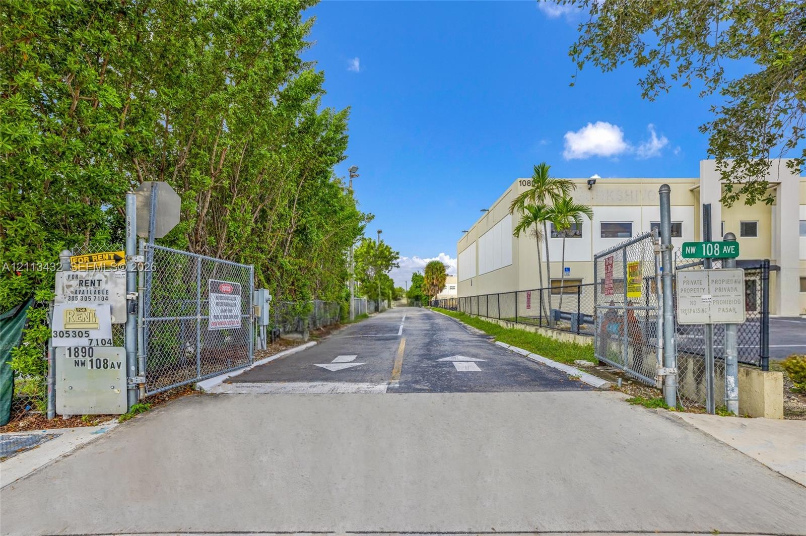 Paved entrance driveway featuring chain-link fencing, dual-gate access, and concrete-surfaced approach