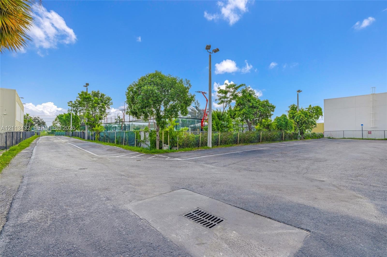 Asphalt parking area featuring perimeter chain-link fencing, stadium-style lighting poles, and mature landscaping