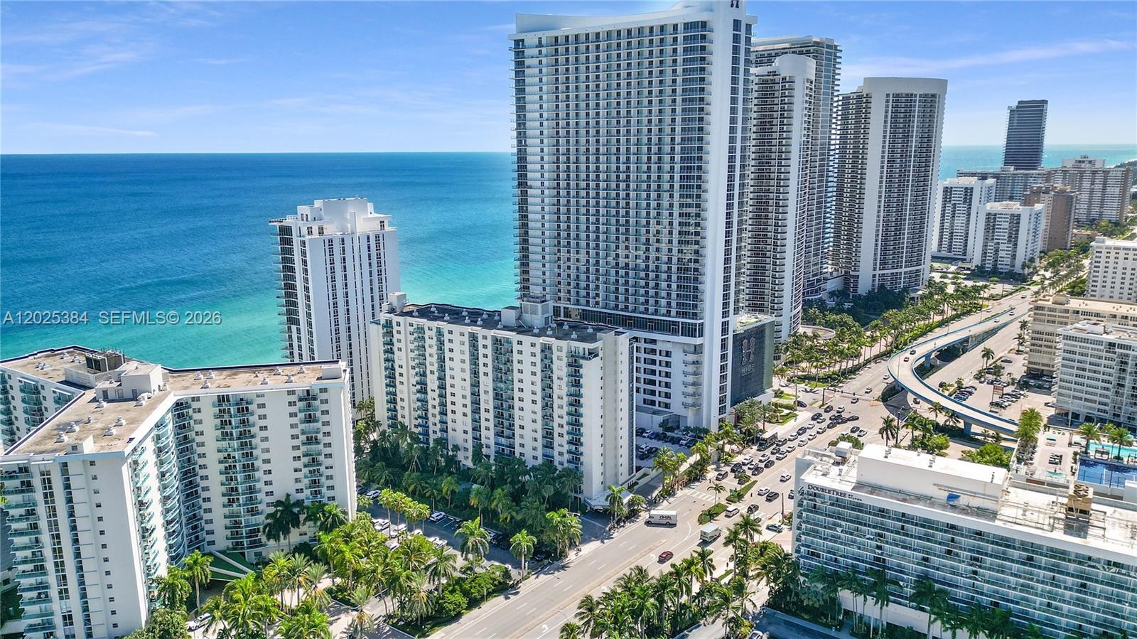 High-rise coastal property featuring white concrete exterior architecture, private balcony tiers, expansive ocean frontage, and manicured palm landsca