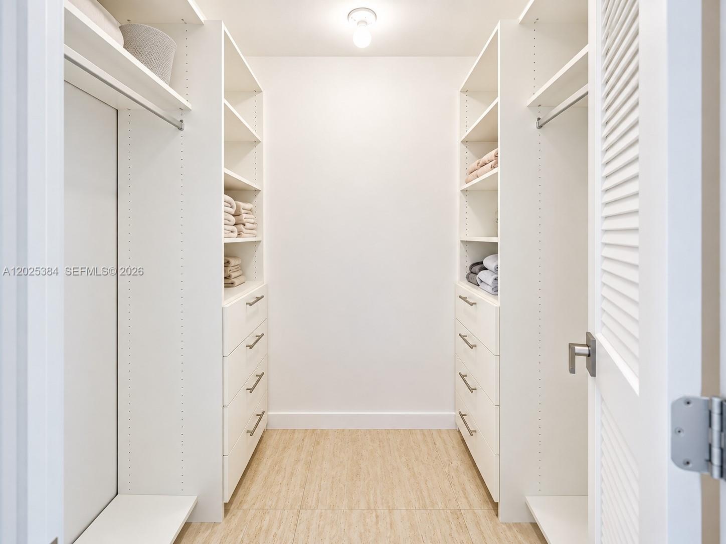 Walk-in storage space featuring built-in white cabinetry, multi-tiered adjustable shelving, integrated drawers with metallic pulls, and wood-finish fl