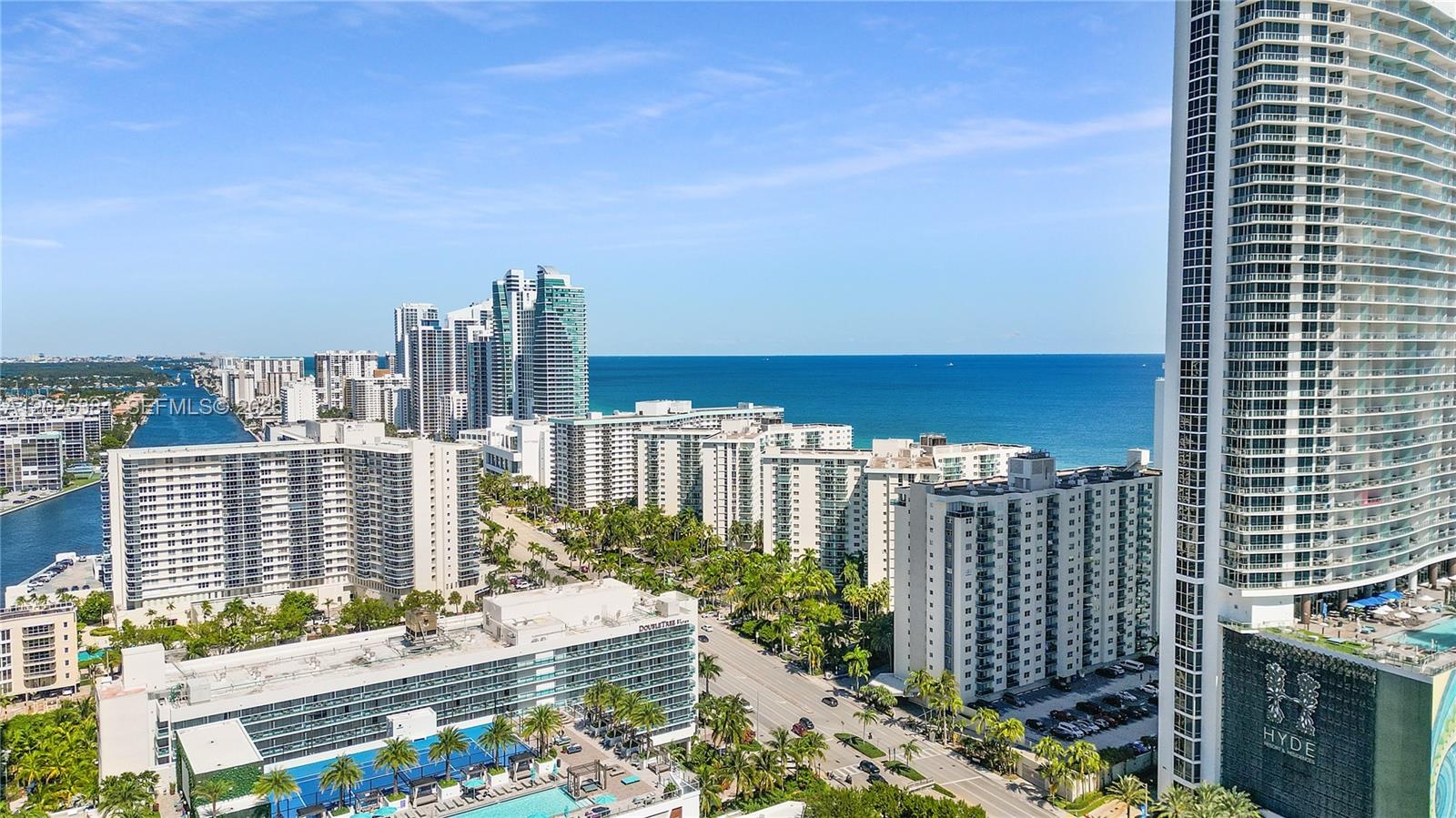 High-rise cityscape featuring multi-story residential structures, coastal proximity, prominent ocean water, and established palm tree landscaping