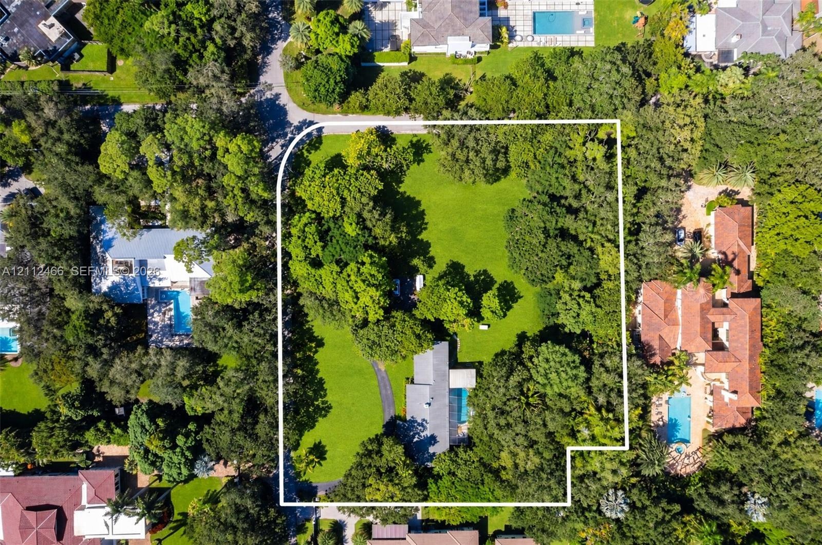 Aerial perspective of a sprawling corner lot featuring mature trees, an expansive lawn, a paved driveway, and an inground swimming pool