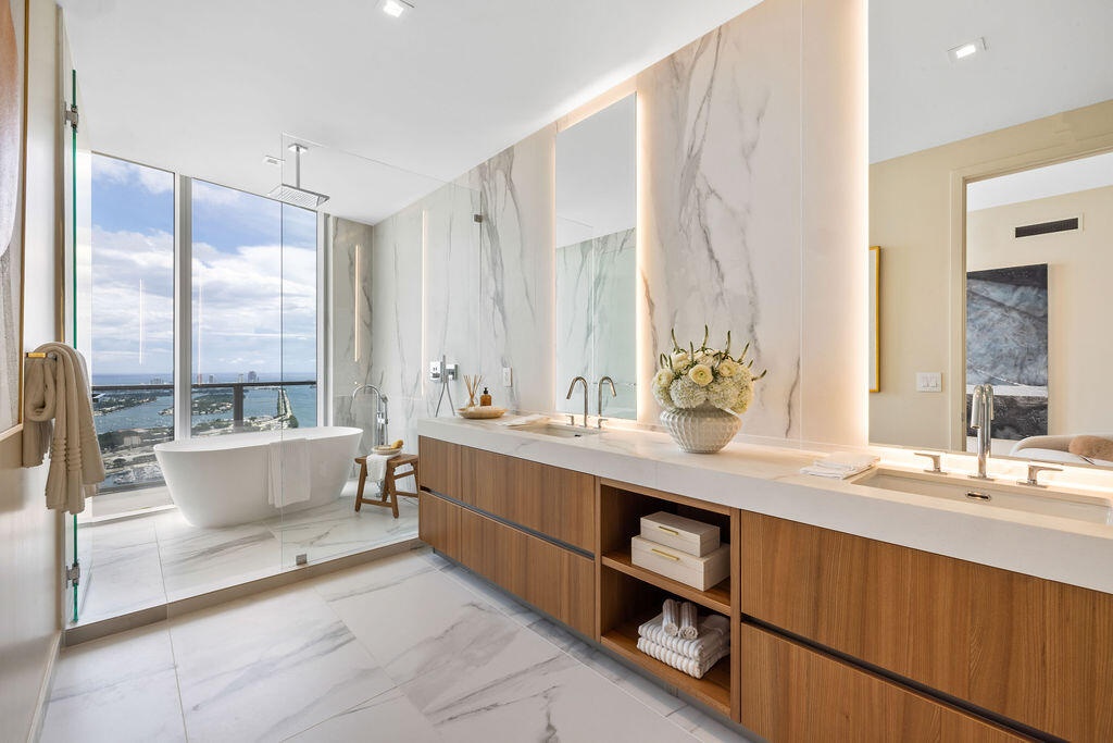 Bathroom featuring floor-to-ceiling stone wall cladding, a floating wood-finish dual vanity with integrated countertop basins, a deep soaking tub, and
