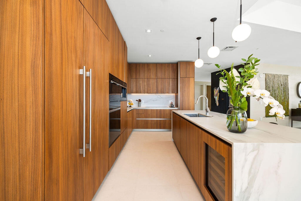 Modern kitchen featuring floor-to-ceiling wood-finish cabinetry, a waterfall-edge stone island, an integrated wine chiller, built-in wall oven, and pe
