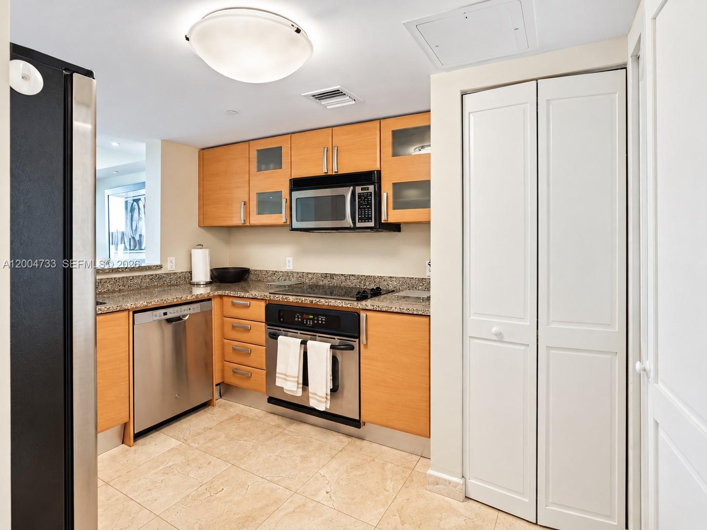 Kitchen featuring natural wood-finish cabinetry, stone-style countertops, stainless steel appliances, and tile flooring
