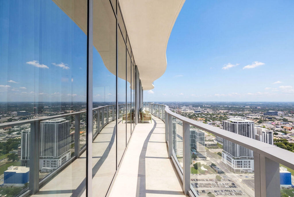 Curved exterior balcony featuring full-height glass curtain walls, concrete flooring, and a sleek metal railing