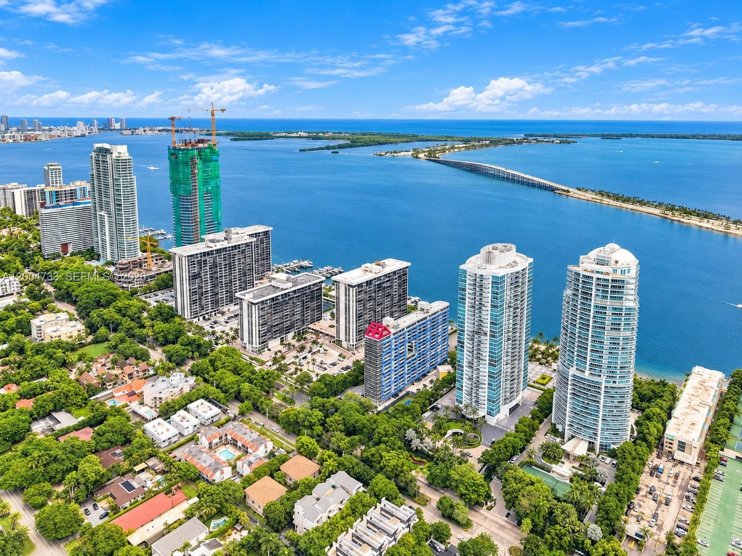 Aerial perspective showcasing high-rise residential architecture, coastal proximity, waterfront orientation, and expansive canopy coverage