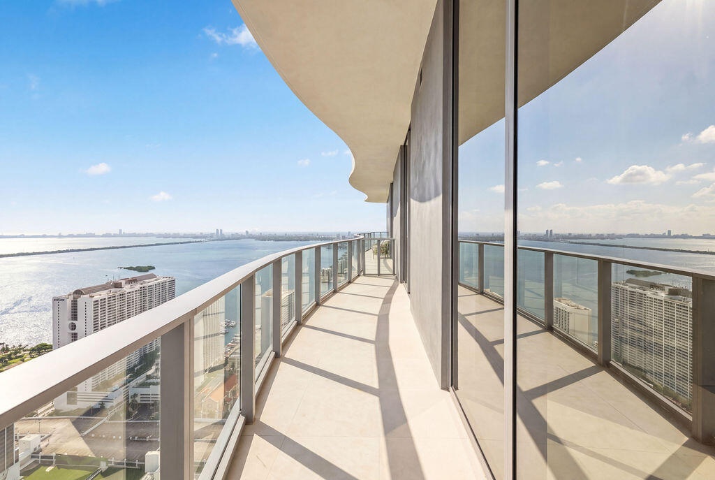 Curved exterior terrace featuring floor-to-ceiling glass panel walls, a metal railing system, and stone-finish flooring