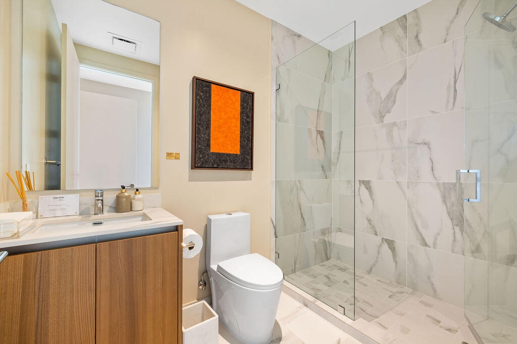 Bathroom featuring a wood-finish vanity with a stone countertop, wall-to-wall mirror, glass-enclosed walk-in shower with floor-to-ceiling stone-style 