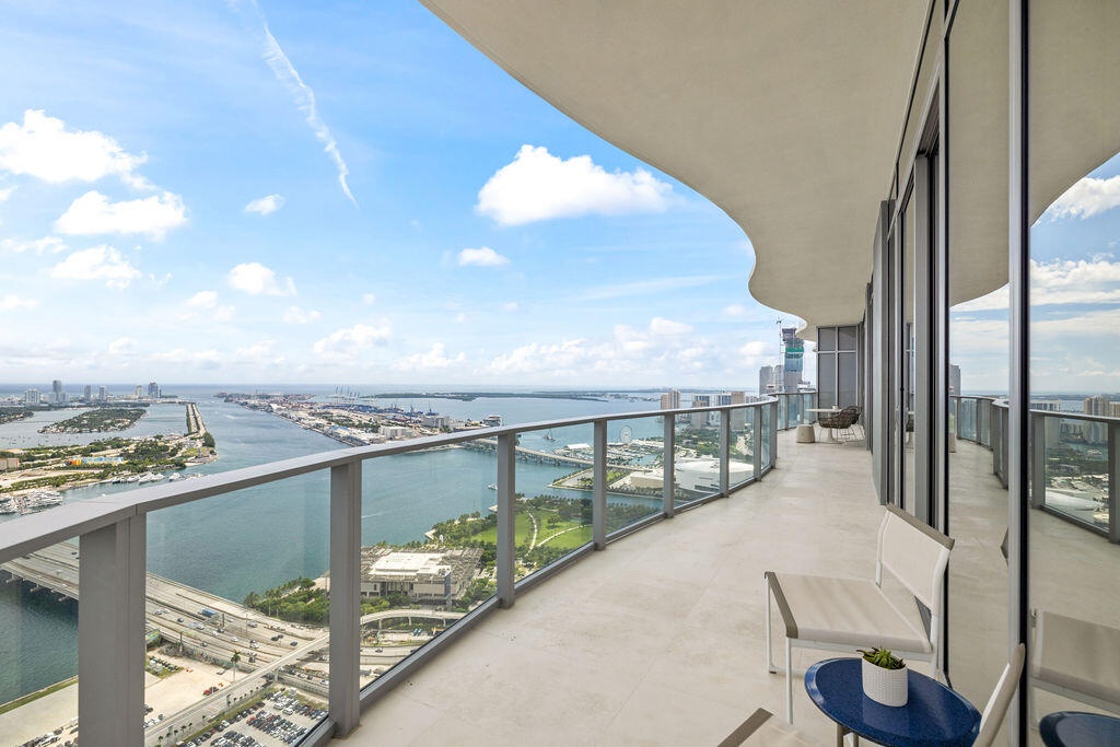Expansive covered balcony featuring glass panel railings, concrete flooring, and full-height exterior windows