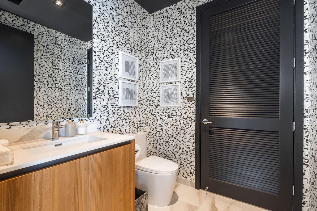 Floating wood-finish vanity with an integrated sink, large-scale wall mirror, patterned wall treatment, and black louvered door