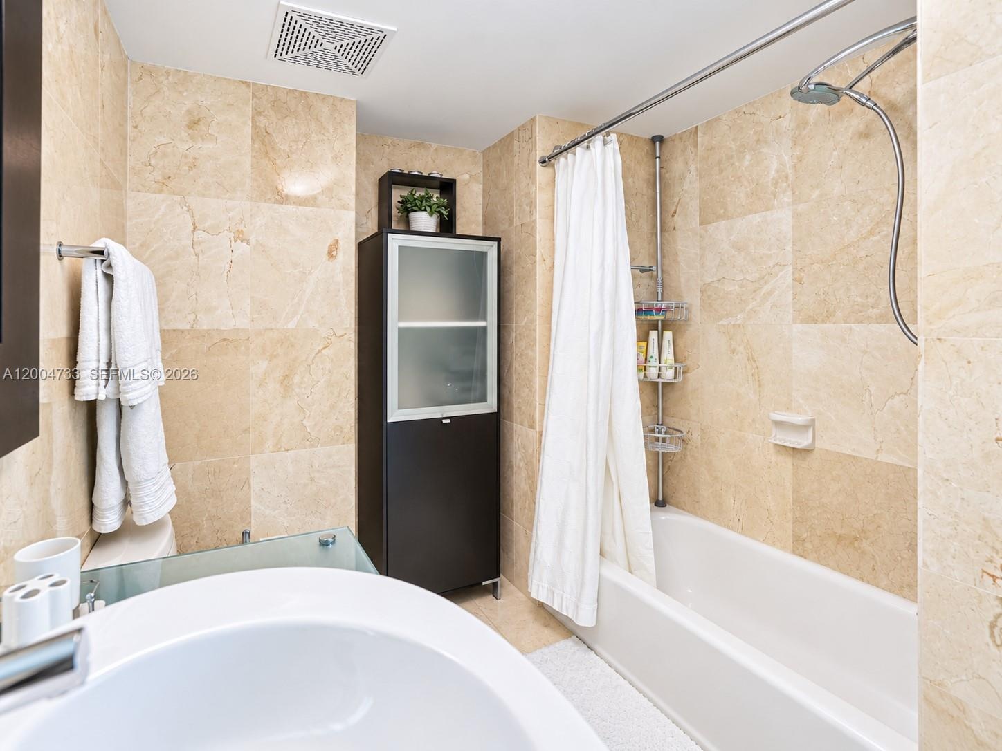 Full-height stone wall tiling, built-in floor-to-ceiling cabinetry with frosted glass panels, a white acrylic soaking tub, and a wall-mounted shower f