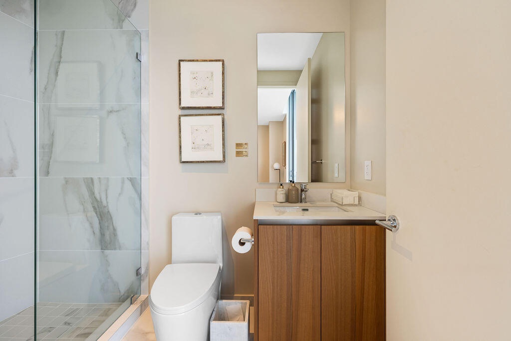 Bathroom featuring a glass-enclosed shower with large-format tile surround, a wood-finish vanity with a stone-surface countertop, an integrated sink, 