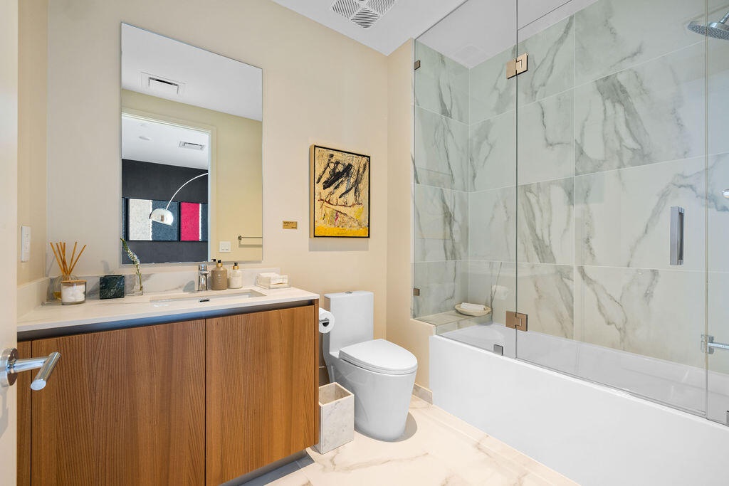 Bathroom featuring a wood-finish vanity with a light-toned countertop, a frameless glass shower enclosure, large-format tile shower surround, and tile