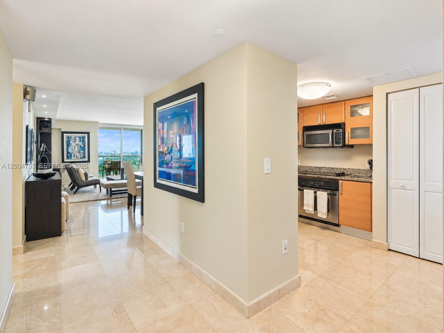 Polished stone flooring throughout, kitchen featuring wood-finish cabinetry, stone countertops, stainless steel appliances, and built-in closet storag