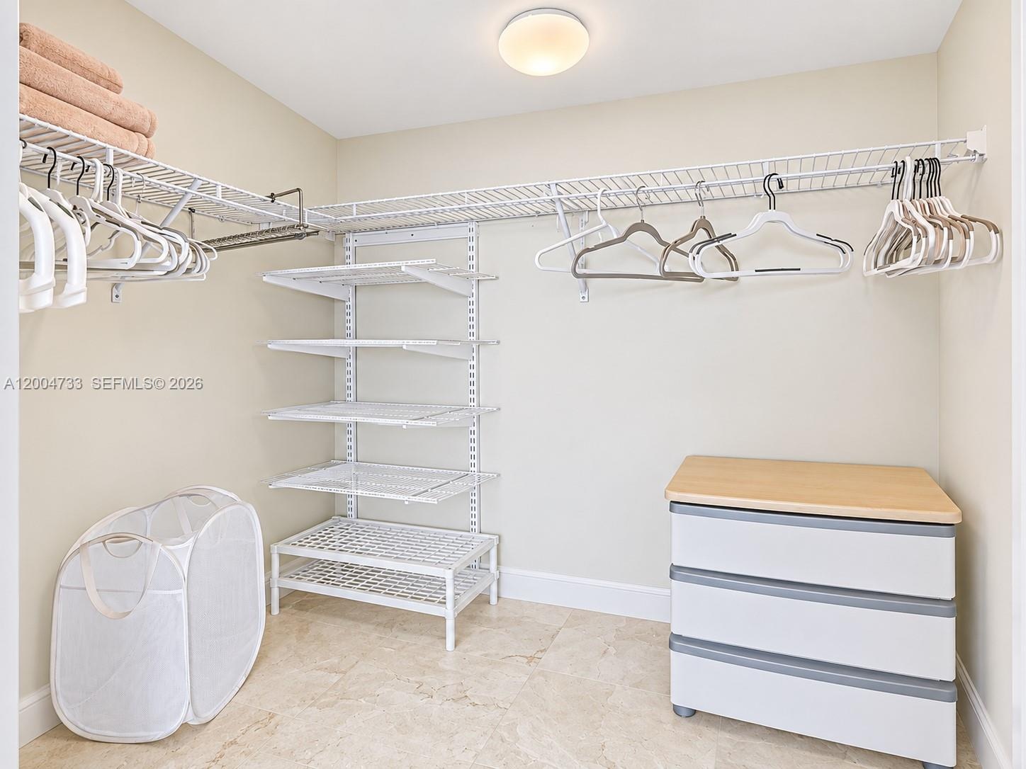 Walk-in closet featuring white wire shelving, wall-mounted adjustable rack system, and stone-finish tile flooring