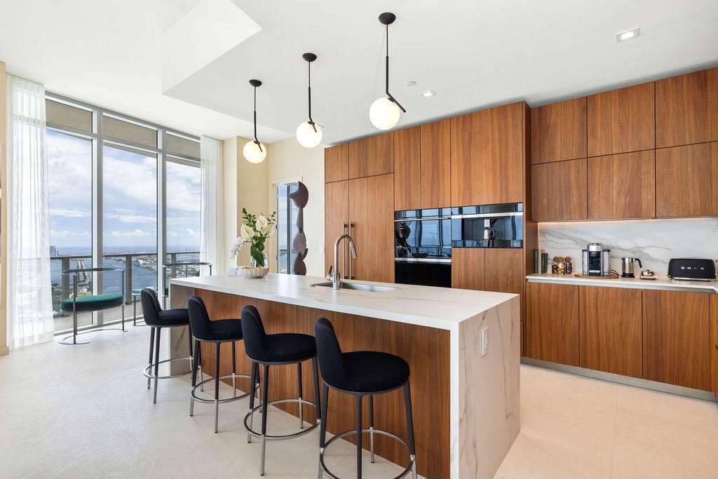 Kitchen featuring flat-panel wood cabinetry, stone-finish waterfall island with an undermount sink, built-in stainless steel appliances, and spherical