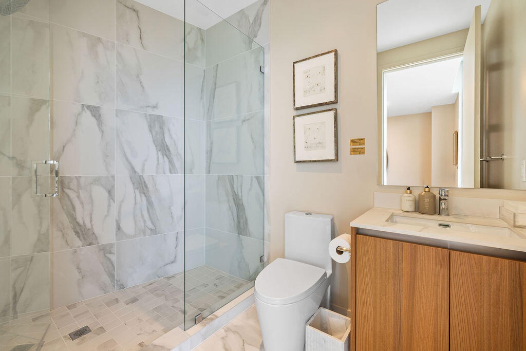 Walk-in shower with floor-to-ceiling stone-finish wall tiles and a glass enclosure, wood-finish vanity with an integrated countertop sink, and a large