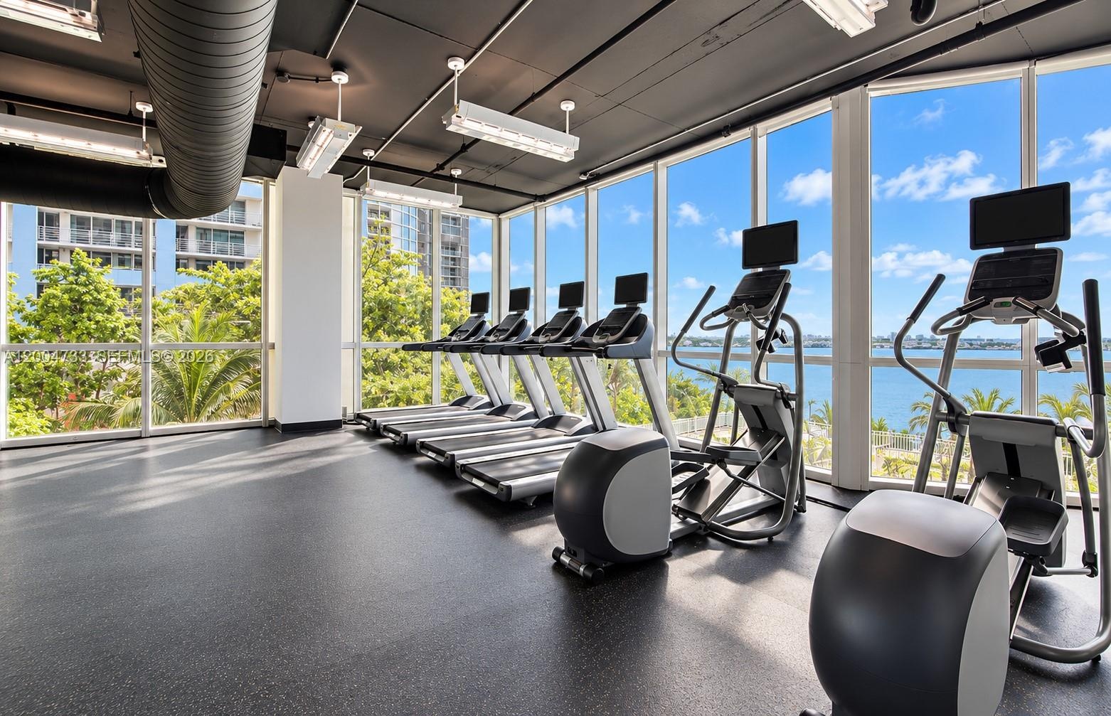 Fitness center featuring floor-to-ceiling windows, industrial-style exposed ceiling, and resilient rubberized flooring