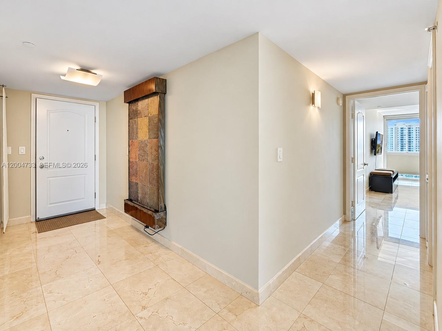 Entryway featuring polished stone tile flooring, a wall-mounted decorative stone-finish water feature, and rectangular flush-mount lighting fixtures