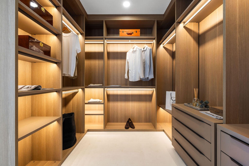 Custom closet featuring light wood-finish cabinetry, integrated LED shelf lighting, tiered hanging rods, and built-in dresser drawers with matte hardw
