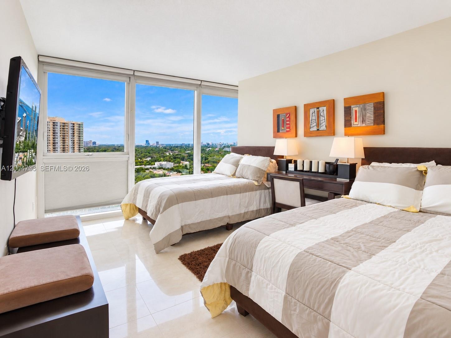 Floor-to-ceiling windows featuring expansive urban and nature scenery, neutral polished tile flooring, and a wall-mounted television console
