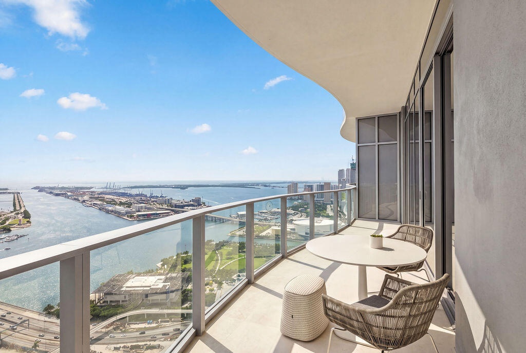 Covered balcony with a curved ceiling, glass panel railing, and expansive water and urban surroundings