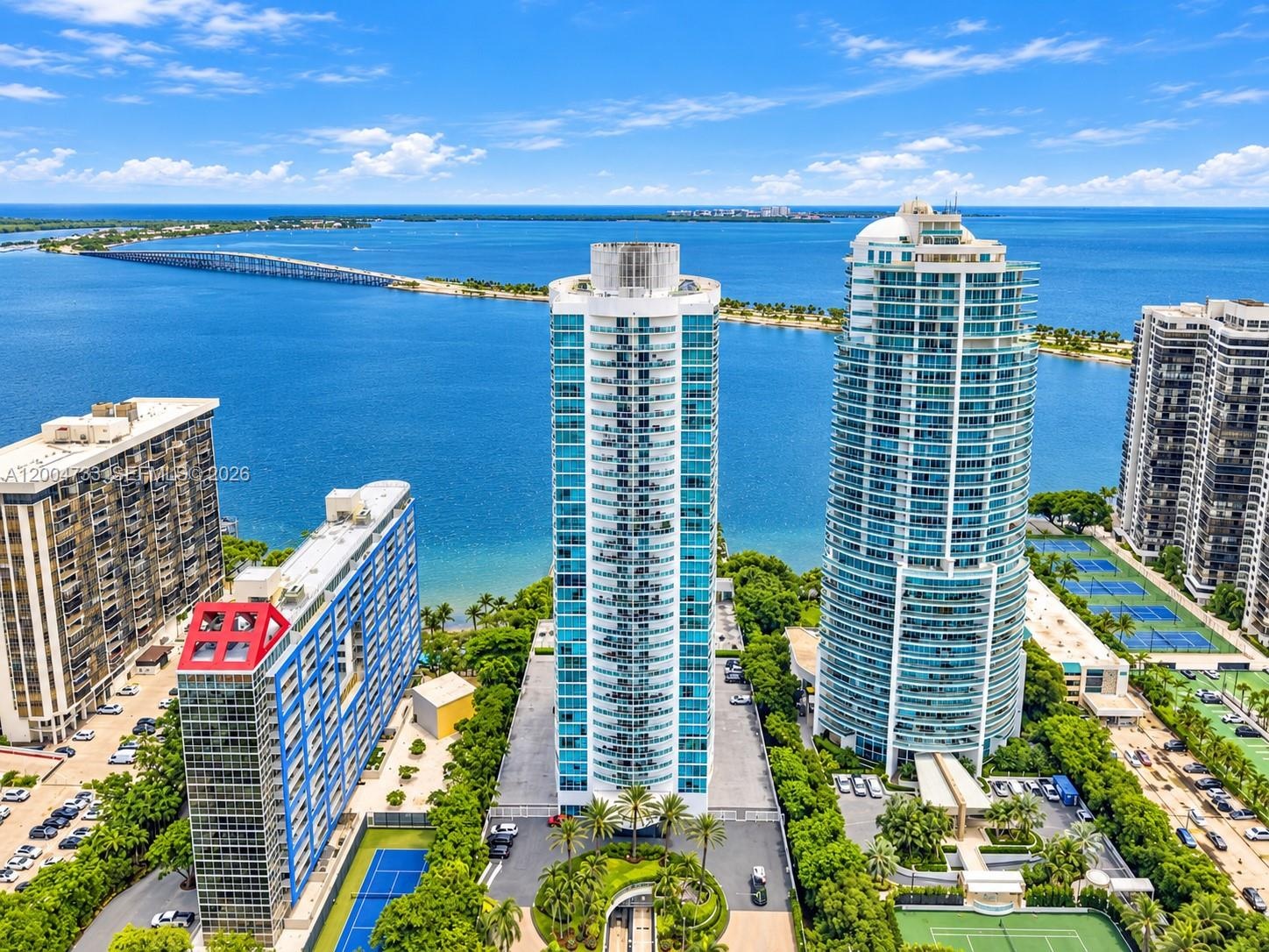High-rise tower featuring glass-paneled balconies, floor-to-ceiling windows, and a waterfront location with immediate access to exterior tennis courts