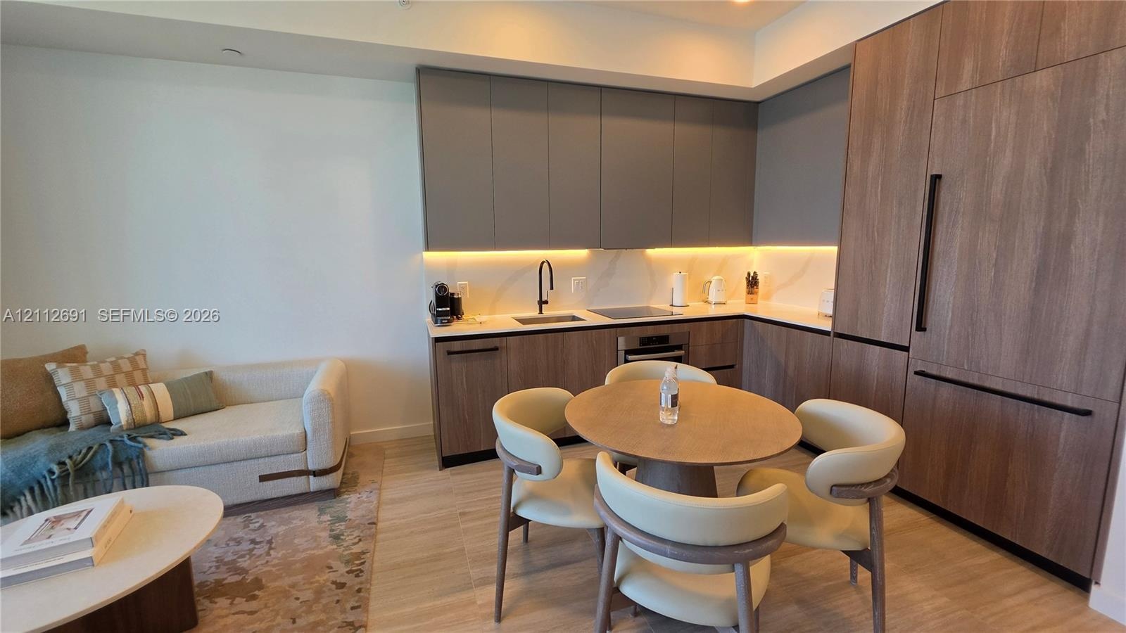 Kitchen featuring flat-panel cabinetry in matte grey and wood-finish, light-toned stone-finish countertops, integrated refrigerator, and under-cabinet