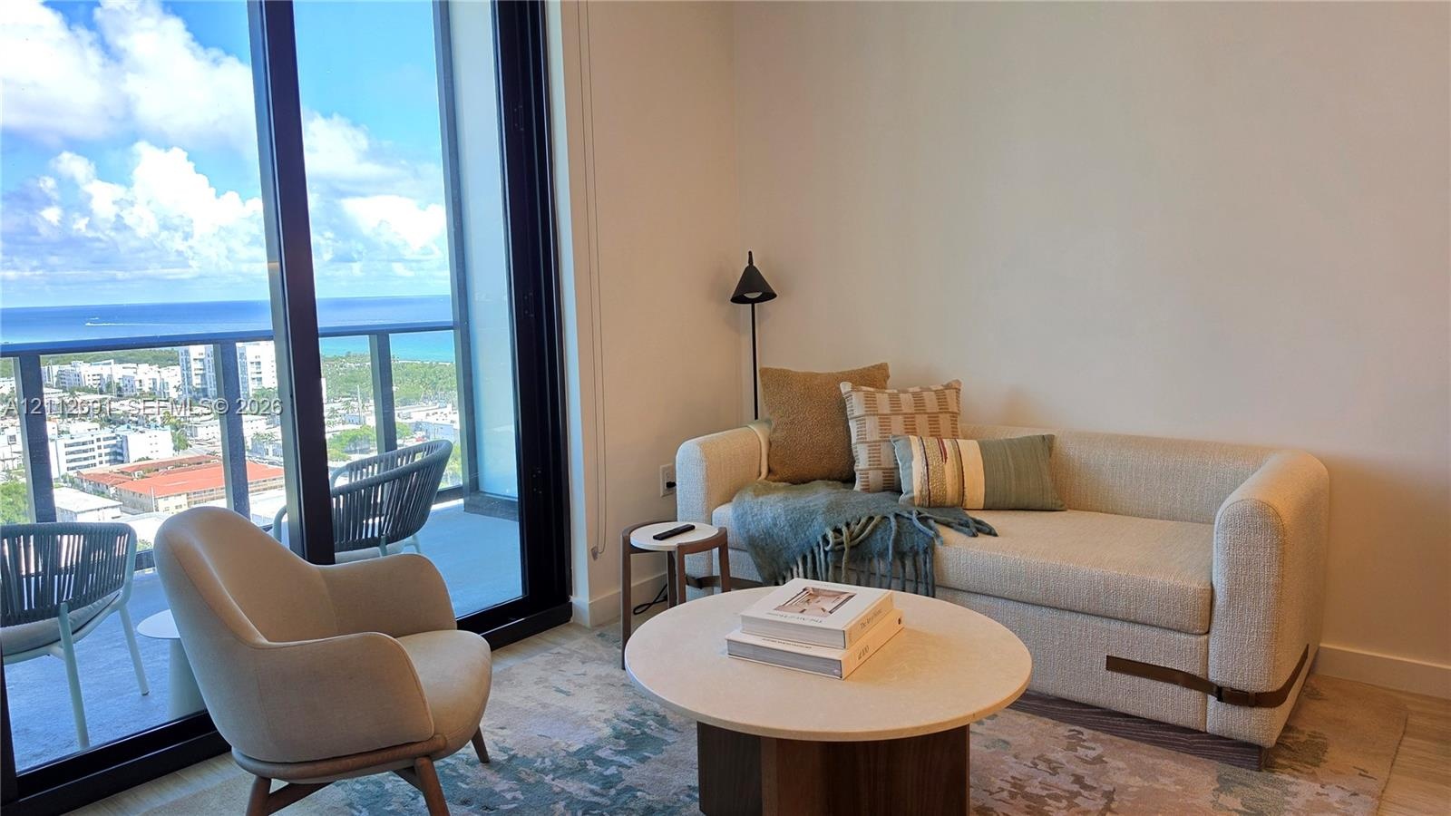 Floor-to-ceiling glass sliding doors, covered balcony with metal railing, and light-toned flooring
