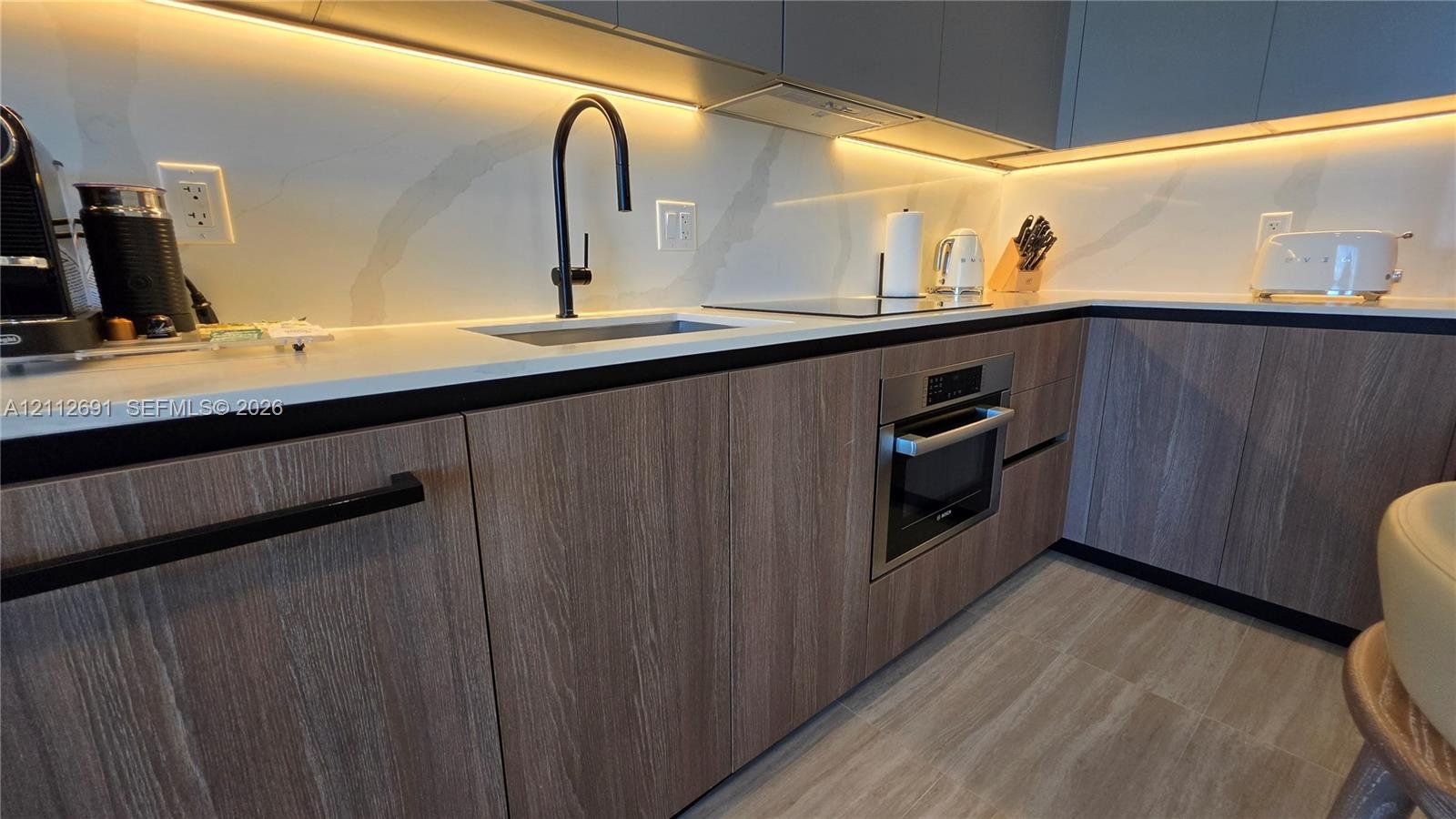 Kitchen featuring flat-panel wood-grain cabinetry, quartz countertops, integrated under-cabinet lighting, a matte black gooseneck faucet, and a stainl